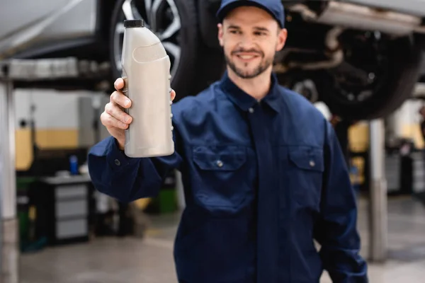 Selective focus of happy mechanic in cap holding bottle with car oil — Stock Photo