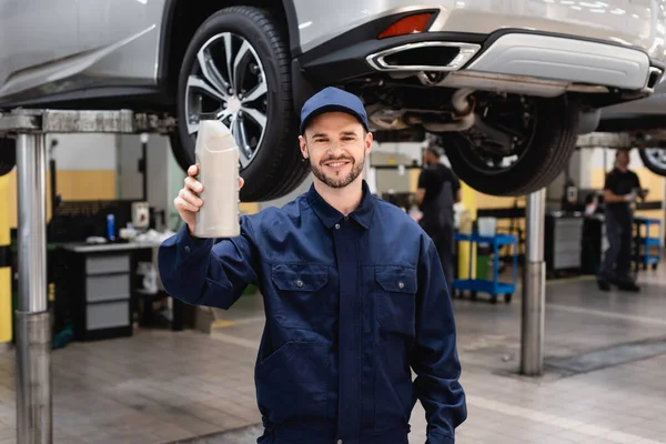 Selective focus of cheerful mechanic in cap holding bottle with car oil — Stock Photo