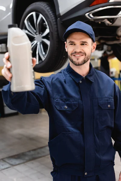 Enfoque selectivo de mecánico feliz en la tapa y botella de retención uniforme con aceite de coche - foto de stock