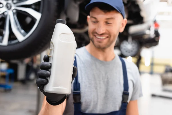Selektiver Fokus des glücklichen Mechanikers in der Mütze mit Blick auf die Flasche mit Autoöl — Stockfoto