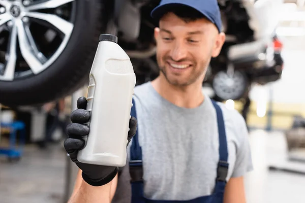 Foyer sélectif du mécanicien heureux dans le bouchon regardant la bouteille avec de l'huile de voiture — Photo de stock