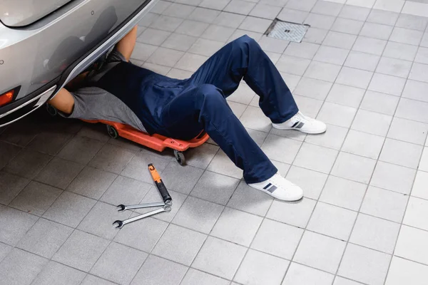 Mechanic lying under car near metallic tools — Stock Photo