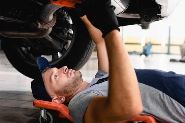 Selektiver Fokus des gutaussehenden Mechanikers liegt unter Auto im Servicecenter — Stockfoto