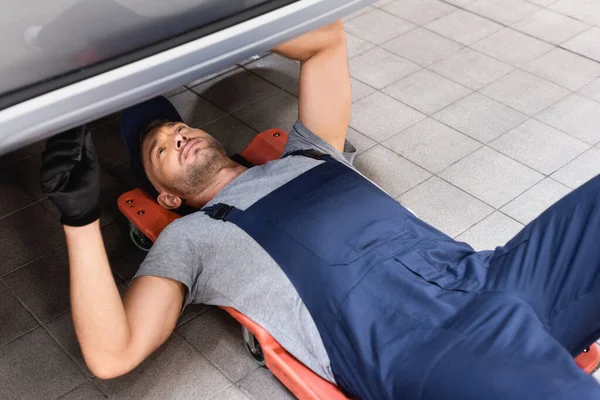 Mecánico guapo acostado debajo del coche en el servicio de coche - foto de stock