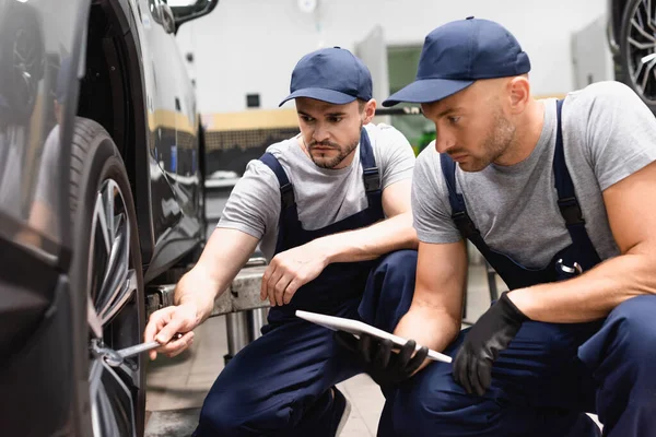 Enfoque selectivo de mecánico celebración tableta digital cerca de compañero de trabajo con llave reparación de automóviles — Stock Photo