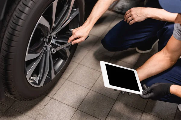 Abgeschnittene Ansicht des Mechanikers, der ein digitales Tablet mit leerem Bildschirm in der Nähe eines Mitarbeiters hält, der mit einem Schraubenschlüssel Auto repariert — Stockfoto