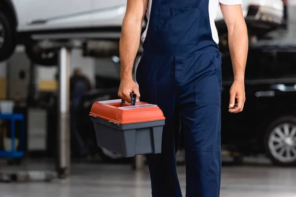 Ausgeschnittene Ansicht eines Mechanikers in Uniform, der Werkzeugkoffer in der Tankstelle hält — Stockfoto