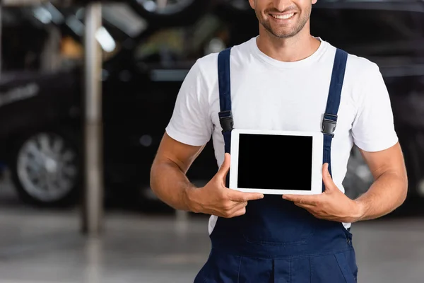 Vista recortada de mecánico feliz en overoles que sostienen la tableta digital con la pantalla en blanco en servicio del coche - foto de stock