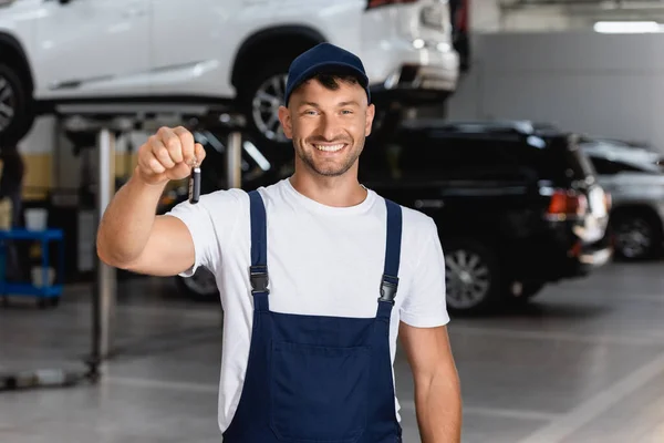 Cheerful mechanic in overalls and cap holding car key — Stock Photo