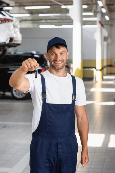 Happy mechanic in uniform and cap holding car key — Stock Photo