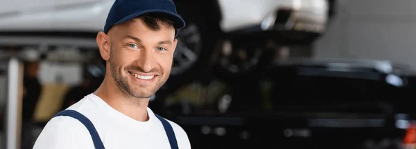 Panoramic orientation of smiling mechanic in cap looking at camera — Stock Photo
