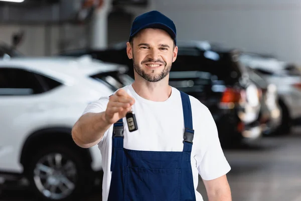 Mecánico alegre en uniforme y la tapa que sostiene la llave del coche — Stock Photo