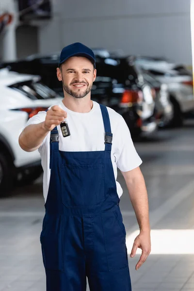 Mecánico sonriente en uniforme y gorra sosteniendo la llave del coche en el taller — Stock Photo