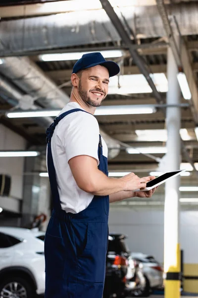 Allegro meccanico in uniforme e cappuccio con tablet digitale con schermo bianco in officina — Foto stock