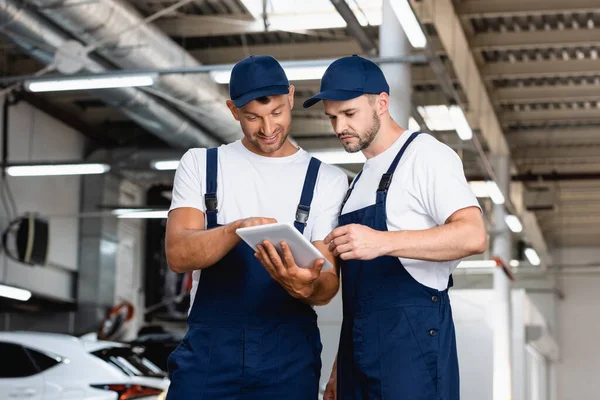 Glückliche Mechaniker in Uniform schauen in der Werkstatt auf digitales Tablet — Stockfoto