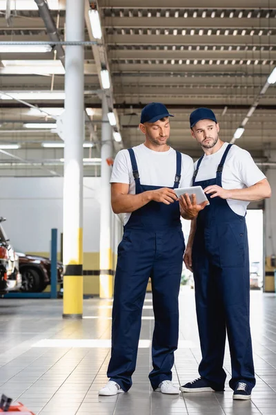 Handsome mechanics in uniform using digital tablet while standing in workshop — Stock Photo