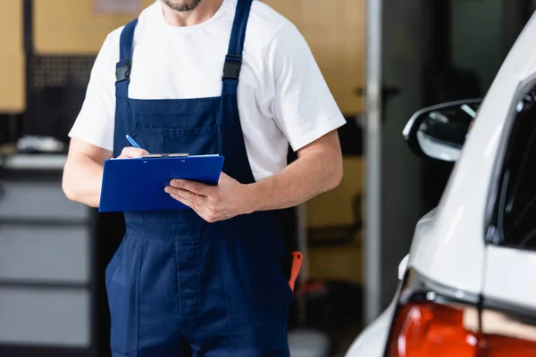 Ausgeschnittene Ansicht eines Mechanikers in Uniform mit Klemmbrett in der Nähe des Autos — Stockfoto