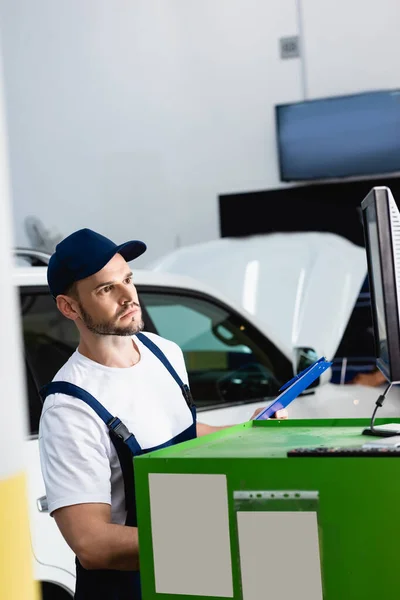 Handsome mechanic in cap looking at computer monitor in workshop — Stock Photo