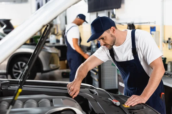 Selective focus of mechanic in cap repairing car near coworker in workshop — Stock Photo