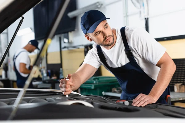 Selective focus of mechanic in cap repairing auto near coworker in workshop — Stock Photo