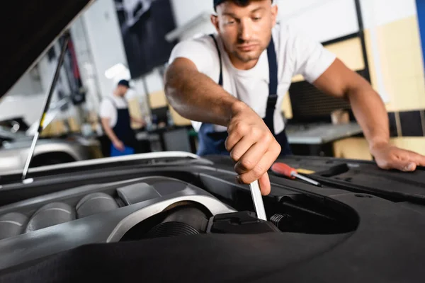 Enfoque selectivo de mecánico guapo en la reparación de la tapa de coche cerca de compañero de trabajo en el taller - foto de stock