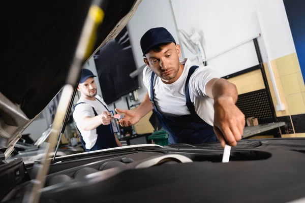 Selective focus of mechanic in cap giving screwdriver to handsome coworker repairing car in workshop — Stock Photo