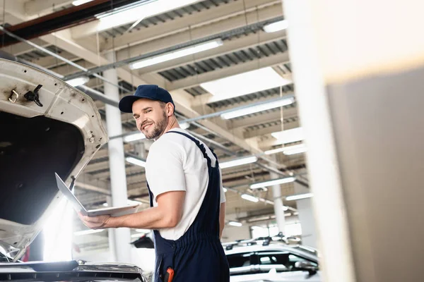 Glücklicher Automechaniker hält Laptop an Tankstelle — Stockfoto