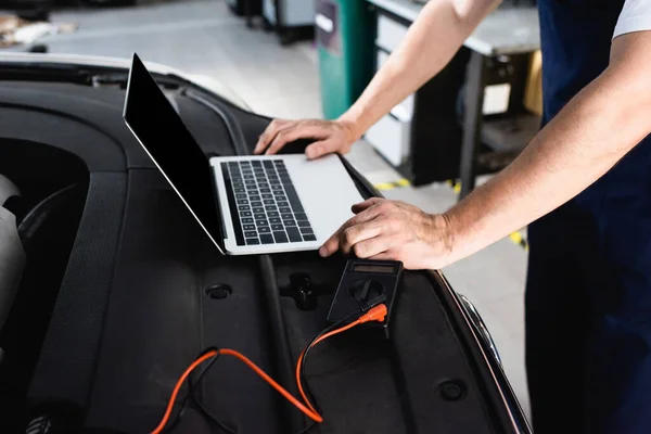 Cropped view of auto mechanic leaning hands on car near laptop and multimeter at service station — Stock Photo