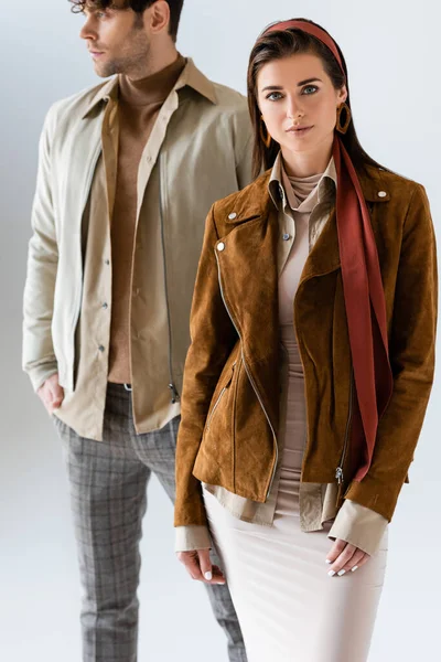 Enfoque selectivo de la mujer atractiva mirando a la cámara cerca del hombre mirando hacia otro lado en ropa de otoño con estilo aislado en gris - foto de stock