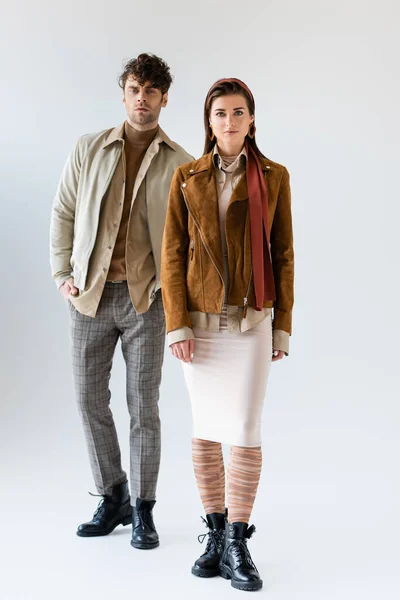 Vista completa de la pareja joven y elegante en ropa de otoño de moda posando en gris - foto de stock