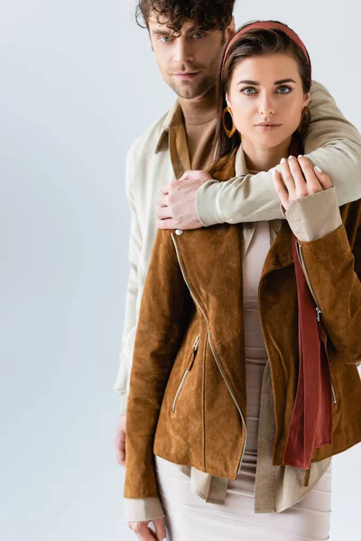 Handsome man hugging stylish woman in suede jacket isolated on grey — Stock Photo