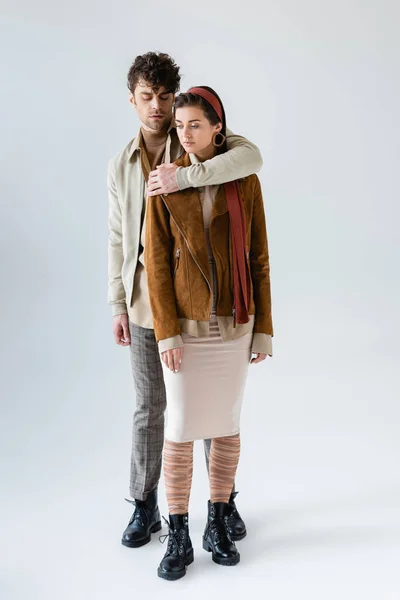 Full length view of stylish man embracing trendy woman in suede jacket isolated on grey — Stock Photo