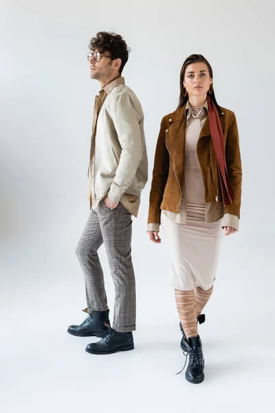 Full length view of fashionable couple posing on grey while man holding hand in pocket — Stock Photo