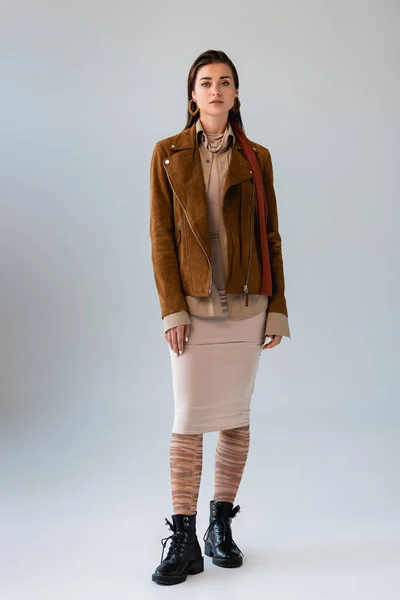 Visão de comprimento total da menina atraente em roupas de outono na moda olhando para a câmera enquanto posando em cinza — Fotografia de Stock