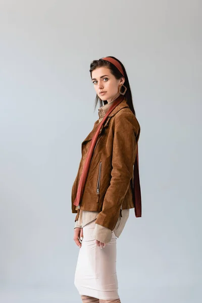 Attractive, fashionable girl in suede jacket looking at camera isolated on grey — Stock Photo