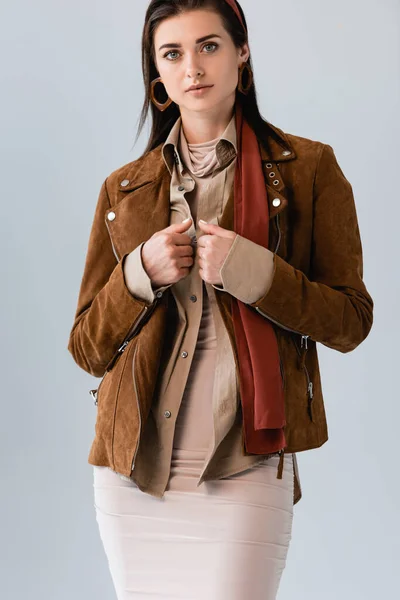 Confident, stylish girl touching suede jacket while looking at camera isolated on grey — Stock Photo