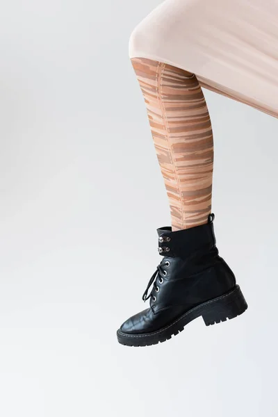 Vista cortada da perna feminina em meias listradas elegantes e bota preta isolada no branco — Fotografia de Stock