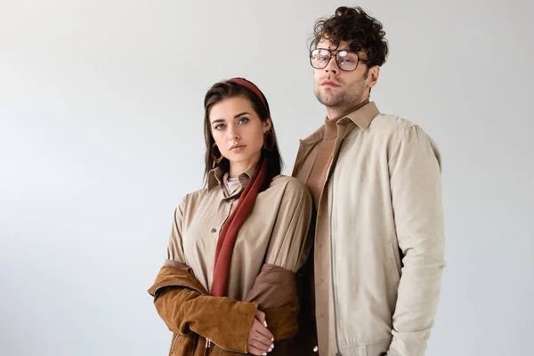 Pareja de moda en ropa de otoño mirando a la cámara mientras posan aislados en gris - foto de stock