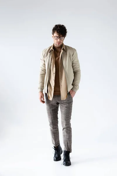 Vista a figura intera dell'uomo alla moda in abiti autunnali in posa con mano in tasca sul grigio — Foto stock