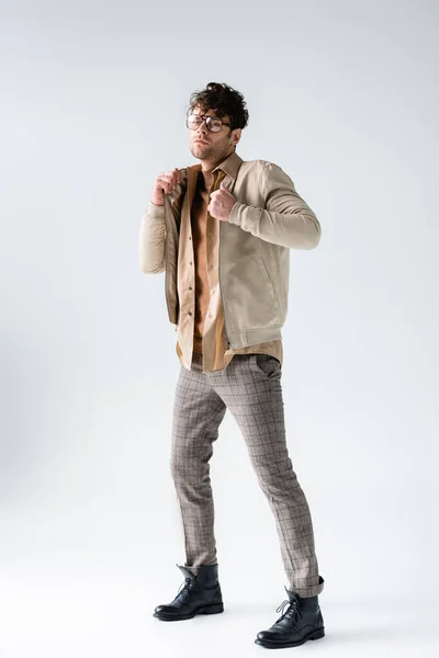 Full length view of stylish man touching jacket while looking at camera on grey — Stock Photo