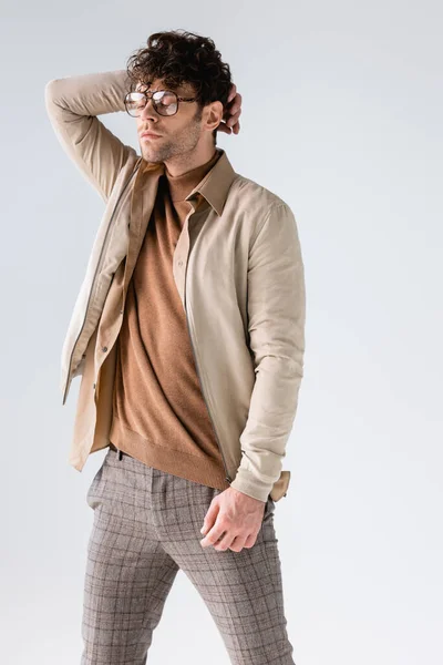 Trendy man in eyeglasses touching hair while posing with closed eyes isolated on grey — Stock Photo