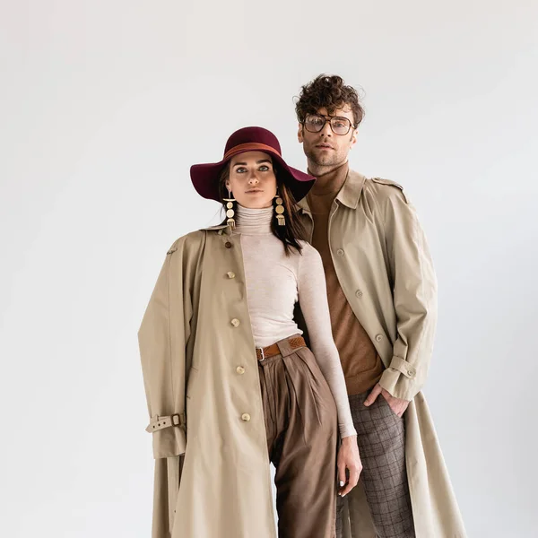 Femme élégante en chapeau et homme à la mode en lunettes posant en vêtements d'automne isolé sur gris — Photo de stock