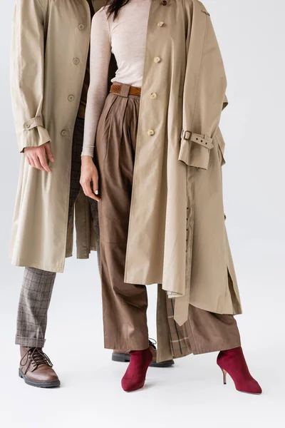 Cropped view of fashionable couple in trench coats and trousers posing on grey — Stock Photo