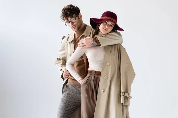 Elegante hombre abrazando a la mujer de moda mientras posa en traje de otoño aislado en gris - foto de stock