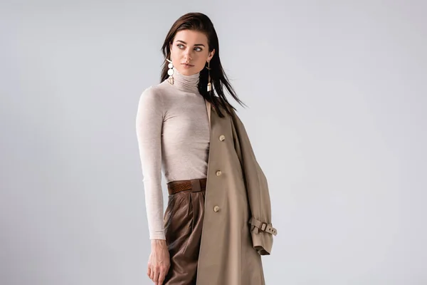Belle, élégante fille tenant trench coat et regardant loin isolé sur gris — Photo de stock