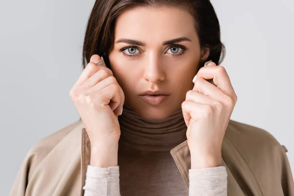 Horizontal image of beautiful girl touching collar of trench coat and looking at camera isolated on grey — Stock Photo