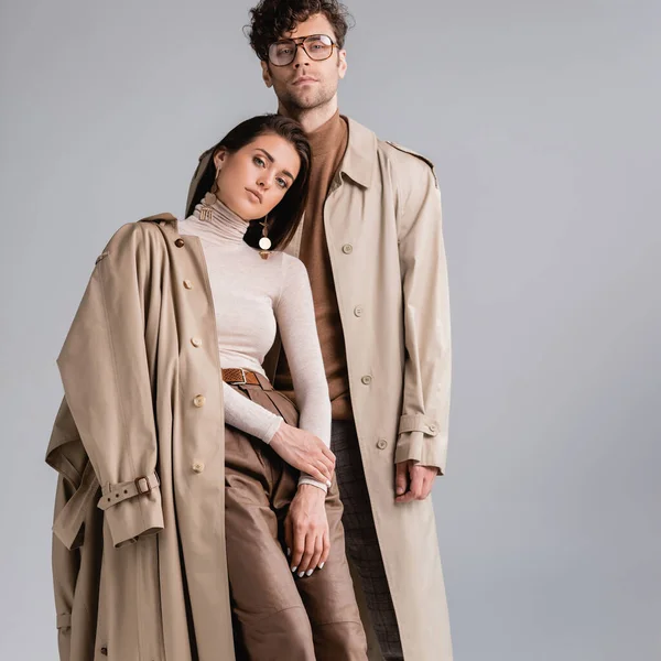 Elegante pareja joven mirando a la cámara mientras posan en ropa de otoño aislado en gris - foto de stock
