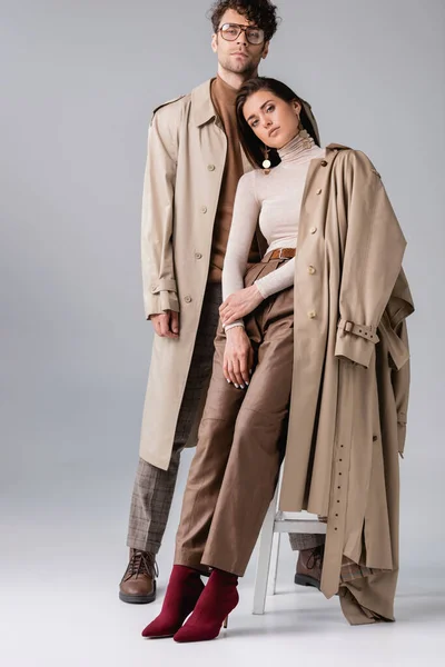 Vista completa de la pareja joven en ropa de otoño de moda mirando a la cámara en gris - foto de stock