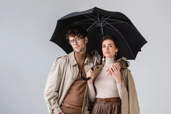 Stylish couple in autumn outfit posing under black umbrella isolated on grey — Stock Photo