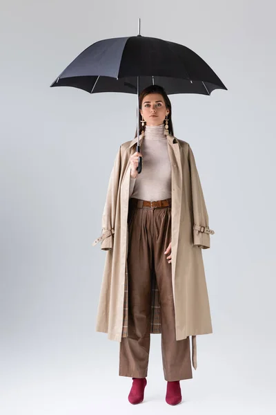 Piena vista lunghezza della donna attraente in abito autunno alla moda in posa con ombrello nero su grigio — Foto stock